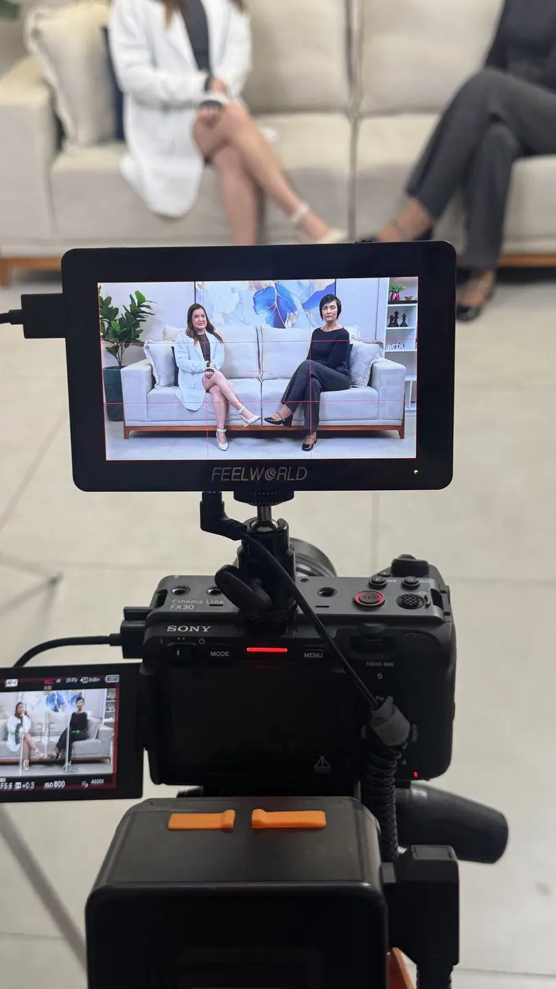 Câmera e monitor de vídeo durante a gravação da entrevista, com as duas participantes enquadradas na tela.